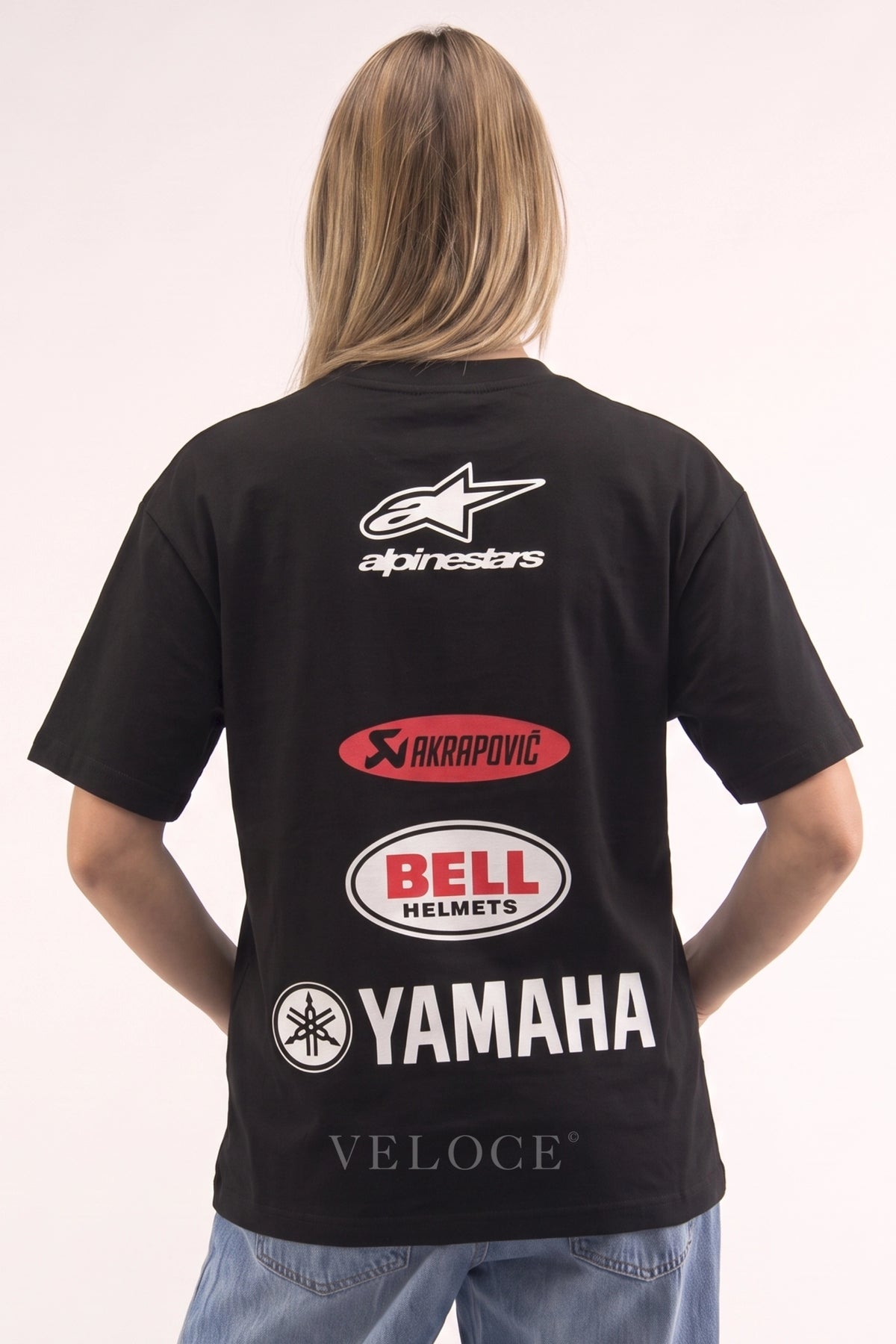 Woman wearing the Alpinestars Racing T-Shirt from behind, showing the Akrapovic, Bell Helmets and Yamaha logos