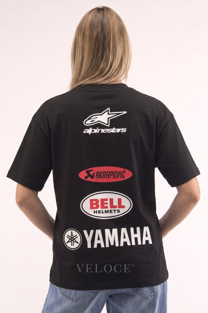 Woman wearing the Alpinestars Racing T-Shirt from behind, showing the Akrapovic, Bell Helmets and Yamaha logos