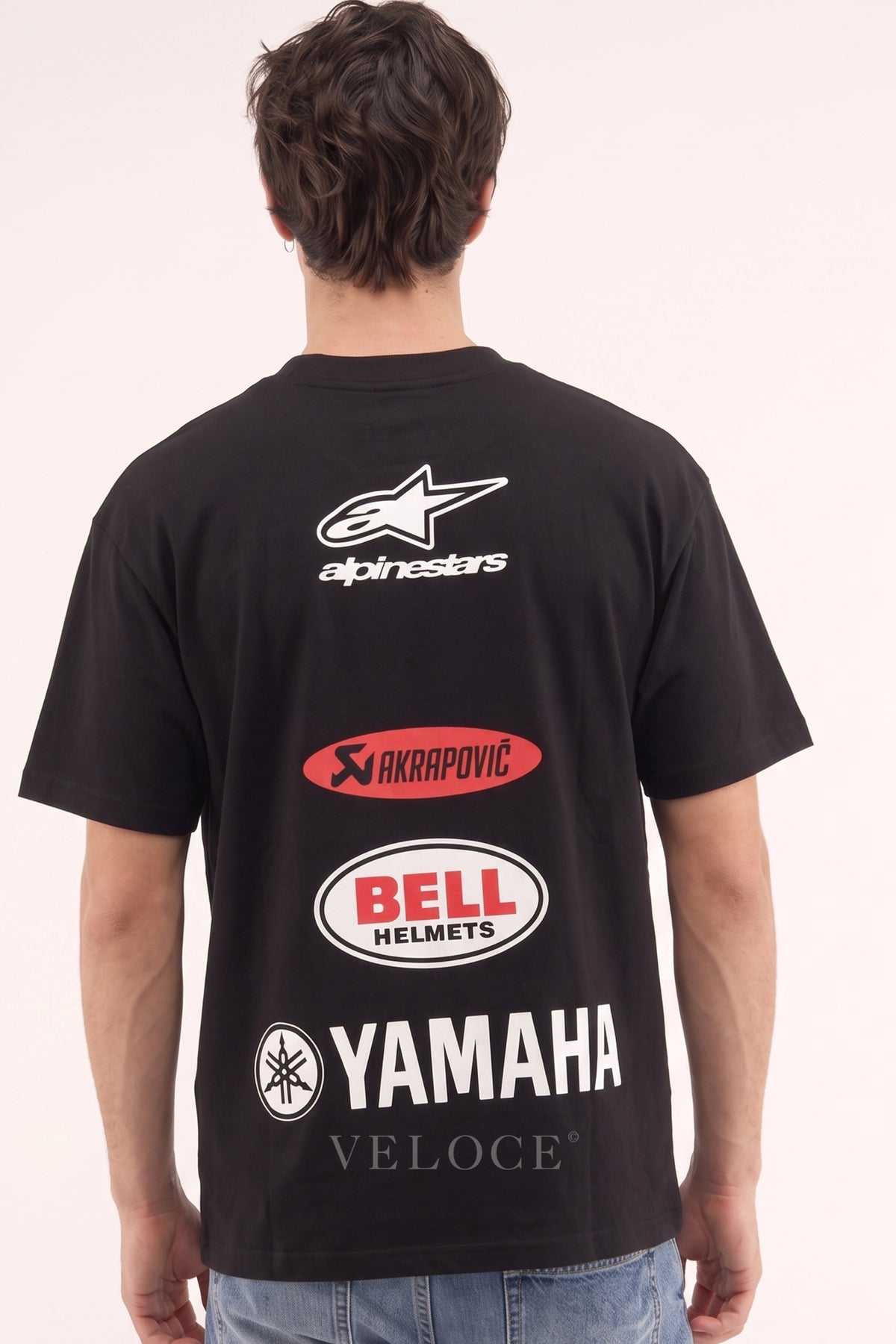 Man wearing the Alpinestars Racing T-Shirt from behind, showing the Akrapovic, Bell Helmets and Yamaha back print
