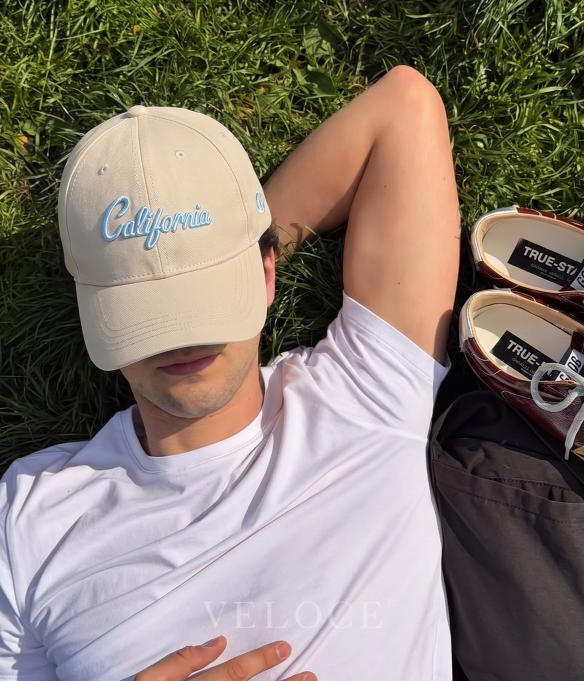 Man wearing the cream California embroidered cap lying on grass