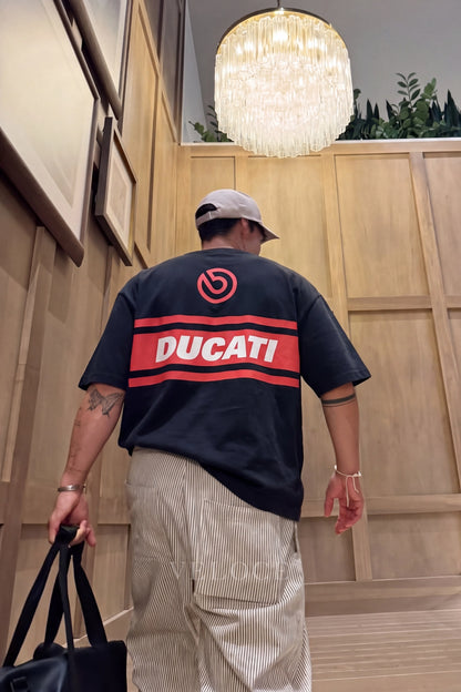 Man in a cap wearing the Ducati Racing T-Shirt indoors, showing the Brembo roundel and Ducati back stripe