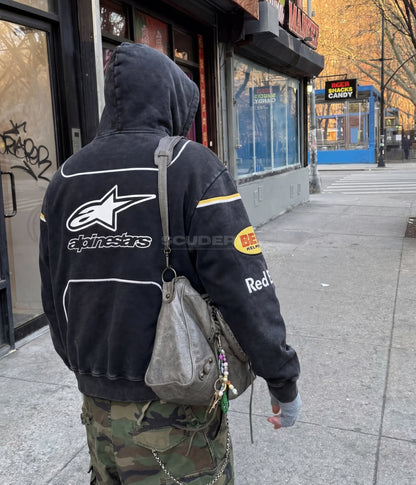 Red Bull Alpinestars Racing Hoodie black washed lifestyle back view man – vintage oversized motorsport sweatshirt with Alpinestars, Bell Helmets and Red Bull back logos, NYC street setting with silver bag