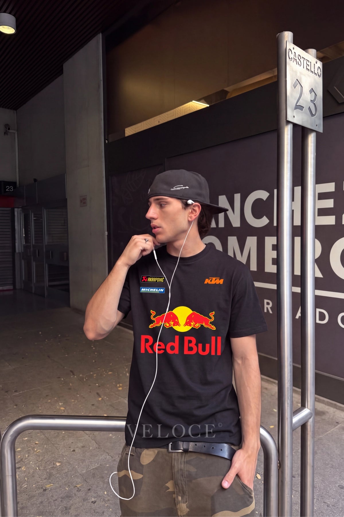 Man in a cap wearing the classic Red Bull Racing T-Shirt at a circuit entrance