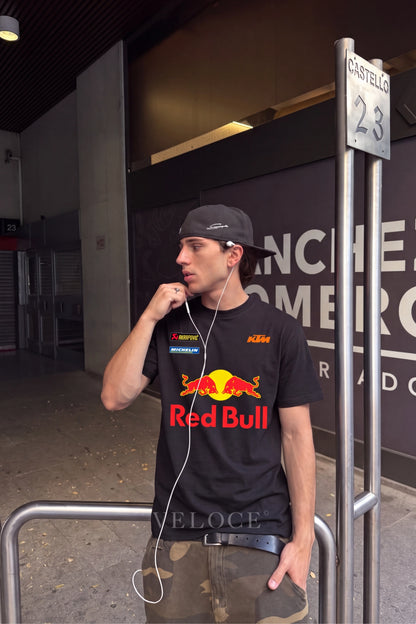 Man in a cap wearing the classic Red Bull Racing T-Shirt at a circuit entrance