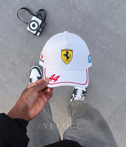Hand holding the white Scuderia Ferrari F1 embroidered cap showing the number 44